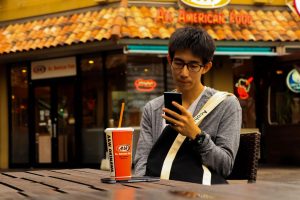 Customer sitting and looking at phone while eating on the patio of a restaurant.