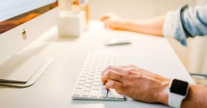 Image of a person's hands typing on a keyboard with part of the monitor showing.